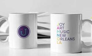 Two white coffee mugs with the JAMNOLA wink logo and the words Joy Art Music New Orleans LA 