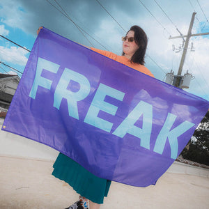 Person holding a purple flag with 'FREAK' printed on it outdoors.