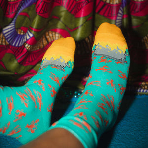 Teal socks with red crawfish and orange firey toes worn by a person sitting on a colorful fabric surface.