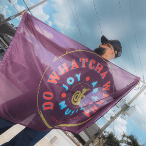 Person holding a maroon flag  that says Do Whatcha Wanna against a blue sky.