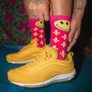 Yellow sneakers with pink socks featuring smiley faces and patterns on a colorful background