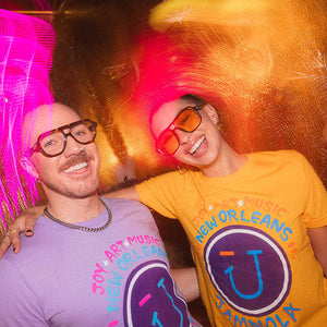 Two people posing together wearing yellow and purple JAMNOLA tees with a vibrant background.