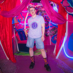 Person standing in a vibrant, colorful room with pink and purple tones wearing Hugo Gyrl JAMNOLA tee in lavender.