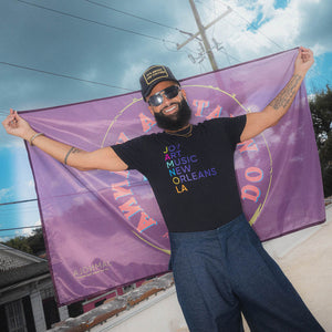 Person wearing a black JAMNOLA tee holding a large maroon flag with text, standing outdoors on a sunny day.