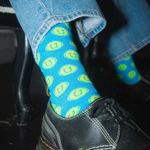 Person wearing blue socks with green and blue Jamnola wink logo pattern.