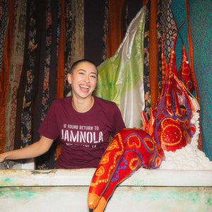 Person wearing a maroon t-shirt that says JAMNOLA, sitting in a tub with a crawfish.
