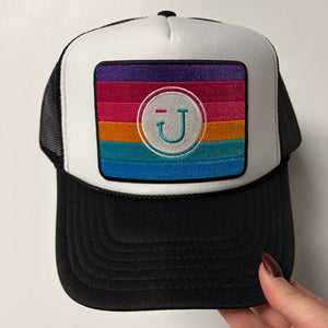 Black hat with a colorful striped patch held by a hand on a white background