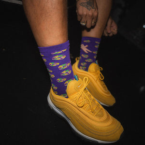 Yellow sneakers with purple socks featuring king cakes on a dark background