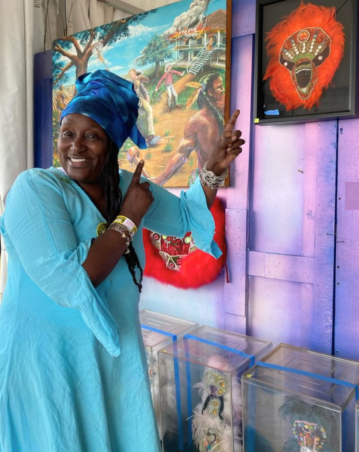 Woman in turquoise dress and blue headscarf posing in front of colorful wall art at Jazz Fest.