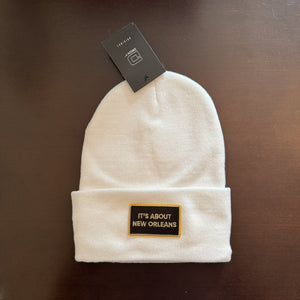 White beanie with a black and gold patch that says 'it's about new orleans'