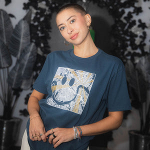 Person wearing a blue t-shirt map with a smile graphic design, sitting in a room with plants.