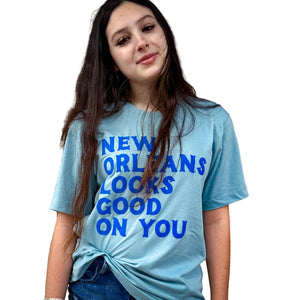 A person wearing a light blue t-shirt with the text 'NEW ORLEANS LOOKS GOOD ON YOU' in bold dark blue letters.
