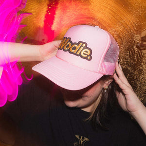 Person wearing a pink cap with 'Wodie' logo against a colorful background