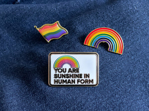 3 rainbow themed enamel pins on dark blue denim