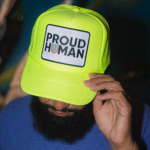 Person wearing a bright yellow cap with 'PROUD HUMAN' text.