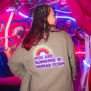 Person wearing a green jacket with a rainbow and text design in a colorful, neon-lit setting.