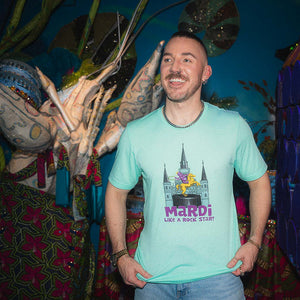 Man wearing a light blue t-shirt with a castle graphic and 'Mardi Like a Rock Star!' text, standing in front of colorful decorations.