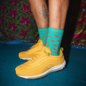 Yellow sneakers with teal crawfish socks on a blue floor.