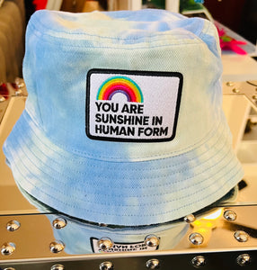 Blue and light seafoam tie dyed bucket hat with a rainbow patch that says You Are Sunshine in Human Form