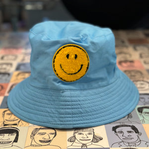Powder blue bucket hat with a textured yellow happy face patch.