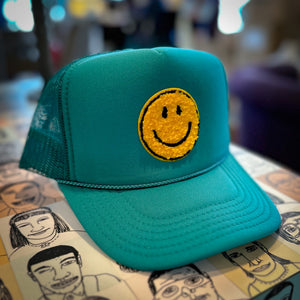 Green trucker hat with yellow smiling face sitting on a table